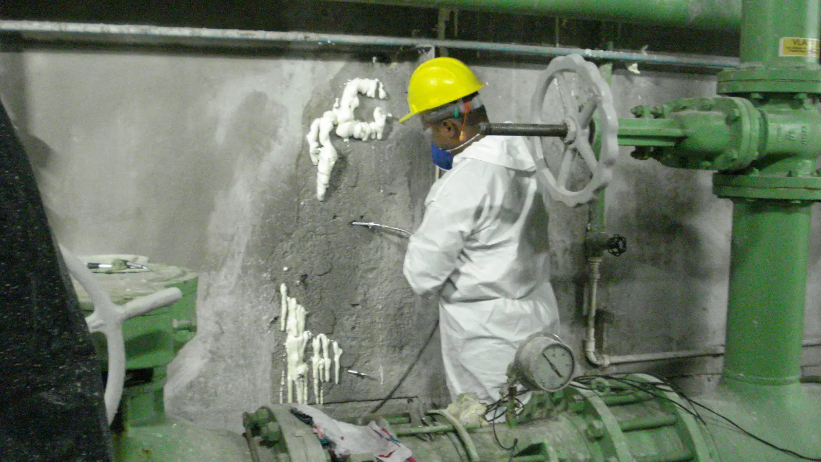 Profissional com macacão branco e capacete injetando poliuretano em parede de concreto com infiltração