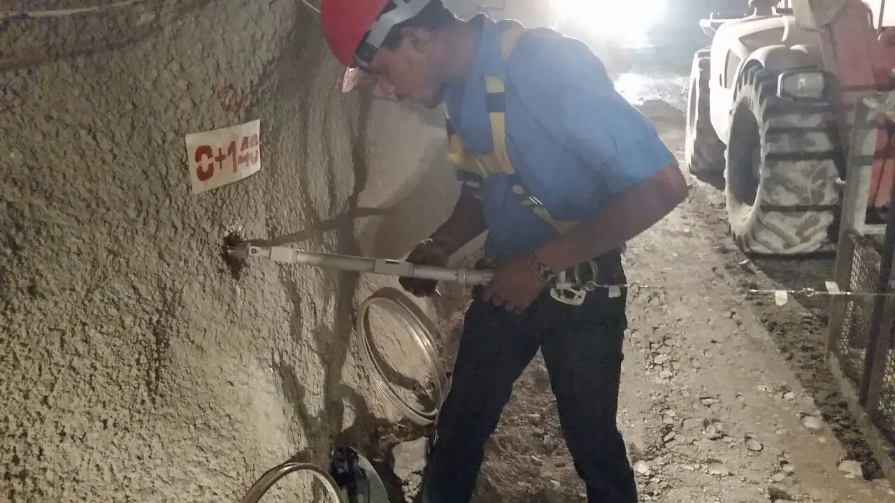 Técnico com capacete e cinto de segurança perfurando parede de rocha para instalação de ancoragem