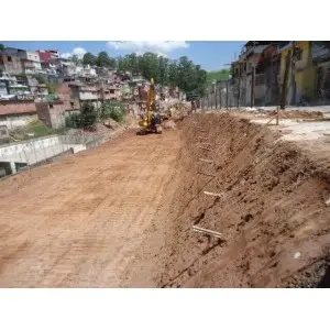 Vala aberta em encosta urbana com equipamento e moradias ao fundo