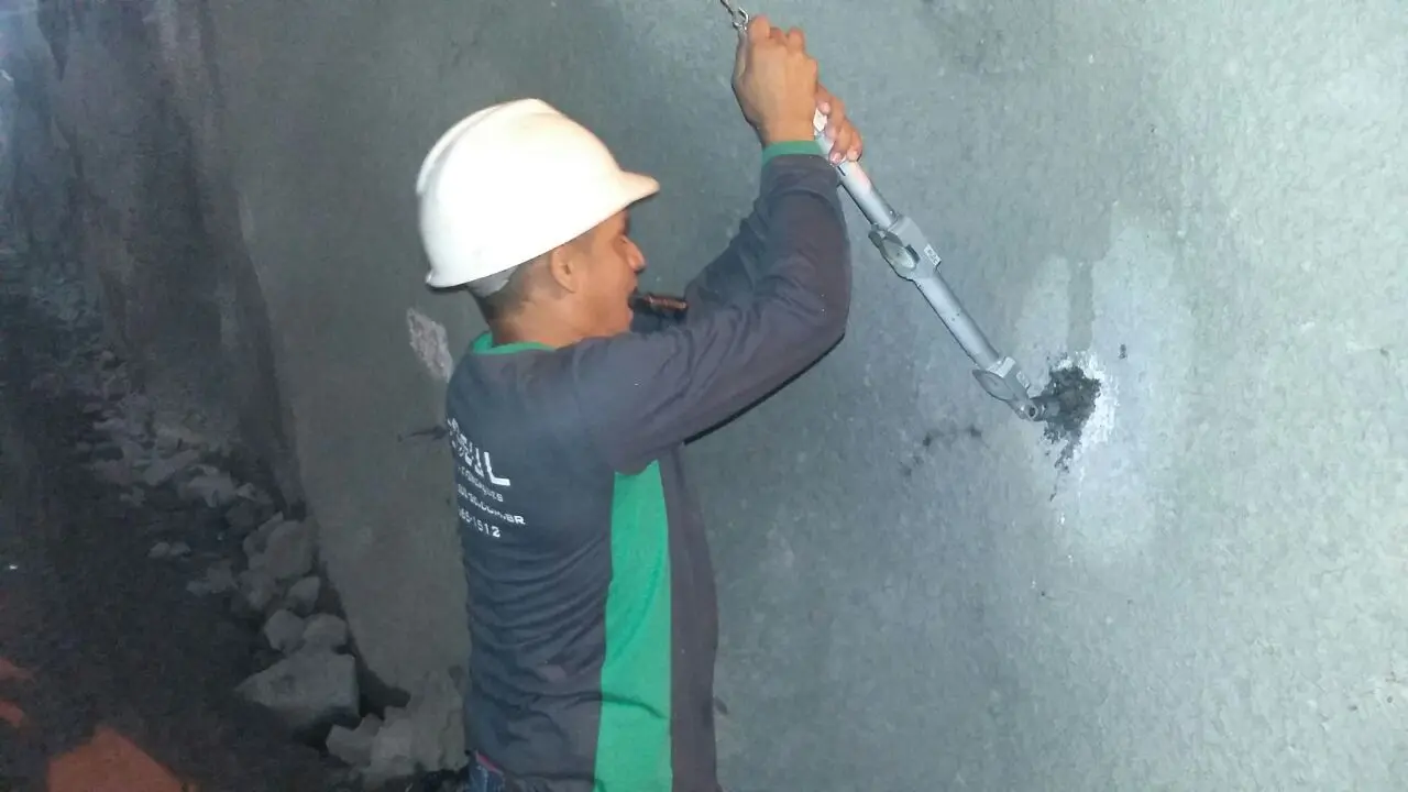 Profissional aplicando material em parede de concreto com equipamento manual