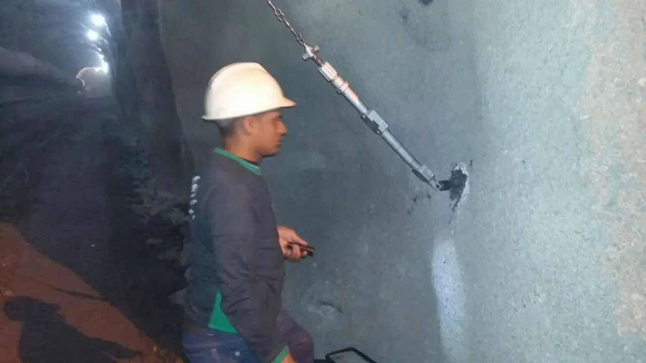 Profissional com capacete branco executando serviço em parede de túnel iluminada